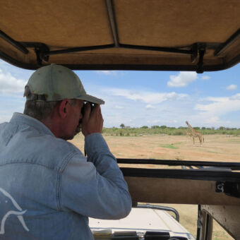 dieren spotten onder het panorama dak man met camera staand in de safari auto met het dak omhoog probeert een giraf die voor de auto staat te fotograferen