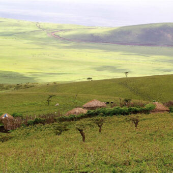 landschap met Masai boma uitzicht van een berg over een masai boma en door de zon verlicht grasland in de verte met heuvels aan de horizon