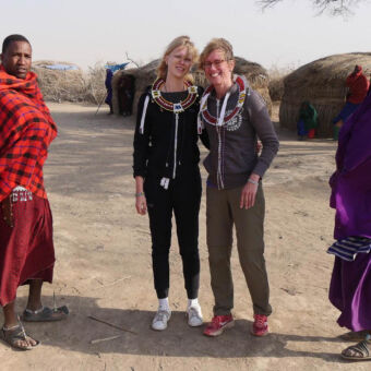 mensen op een excursie in een Masai dorpje met twee masai in felgekleurde kleding