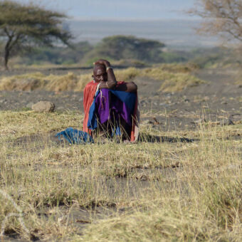 Masai vrouw zittende Masai vrouw in kleurrijke kleden tussen het gras