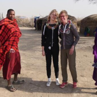 mensen op een excursie in een Masai dorpje met twee masai in felgekleurde kleding