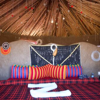 opgemaakt bed in een masai lodge. wwitte lakens en felgekleurde dekens en overal kraaltjes tanzania