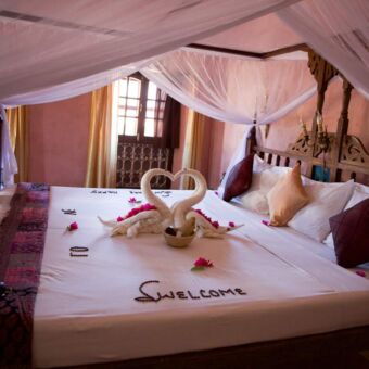 mooi opgemaakt bed met handdoeken gevouwen in de vorm van twee zwanen en welcome gemaakt van roze blaadjes op lodge in zanzibar