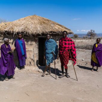 masai familie met volwassen mensen staand bij hun boma. Die is gemaakt van klei en met een rieten dak