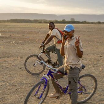 tanzaniaanse jongen die een v teken maakt en een man stilstaand met hun fiets