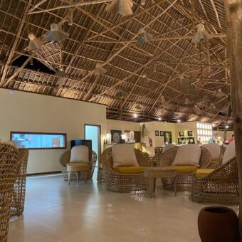 binnekant van een accommodatie op zanzibar met hoge plafonds met rietgedekt. op de voorgrond een mooi gedekte grote tafel voor het diner