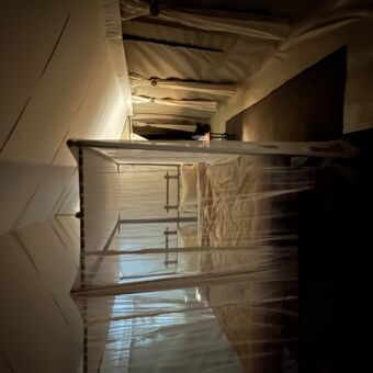 je kijkt door het gaas in de safaritent waar een groot bed staat mooi opgemaakt met witte lakens.