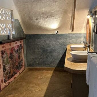 badkamer bij sunshine marine lodge op zanzibar. Het dak loopt schijn en is wit de muren grijs mat en verder twee wastafels op een mooie houten blad