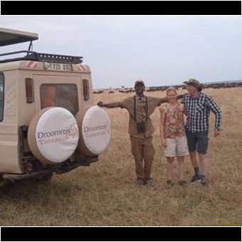 op de voorgrond de safariauto van droomreis tanzania met daarnaast de gids en twee gasten tijdens hun huwelijksreis. op de achtergrond to aan de horizon een grote groep gnoes tijdens de grote migratie op de serengeti