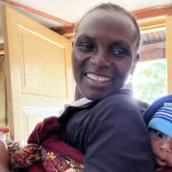 lachende Tanzaniaanse vrouw met een baby op haar rug gebonden