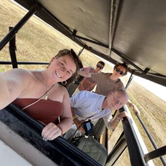 selfie van een familie die op safari is en onder het open dak staan met daarachter de Serengeti