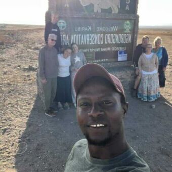 Selfie van 7 gasten en hun gids bij het bord van de Ngorongoro Kratewr