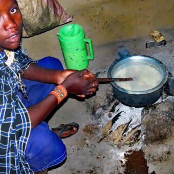 Activiteit rondreis Tanzania. Bezoek aan een Masai Boma waar een vrouw mais pap kookt op een vuurtjes. Reisverslag safari Tanzania