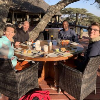 Gasten lunchend en zittend aan een ronde tafel met hun gids bij Lake Masek in Ndutu. Dit is een van de accommodaties tijdens hun safari rondreis door Tanzania