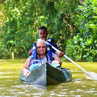 Vrouw die in een kano zit met daarachter een gids die rondpeddels op Lake Duluti in Tanzania