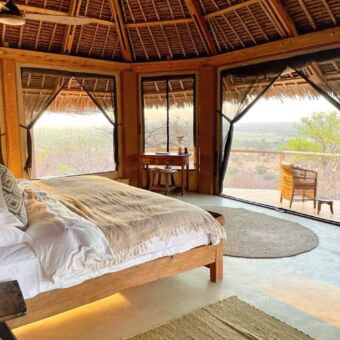 Luxe suite met een groot bed met wittel lakens, houten vloer, rieten dak, ramen van gaas en een mooie veranda met twee stoelen