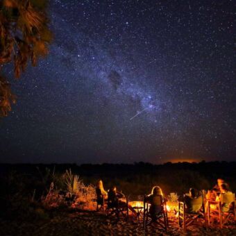 Mensen zitten bij een kampvuur in Ruaha onder een hemel vol met sterren