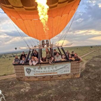 Een groep mensen in de mand van een heteluchtballon die over de uitgestrekte savanne van de Serengeti zweeft, met de brander in actie.