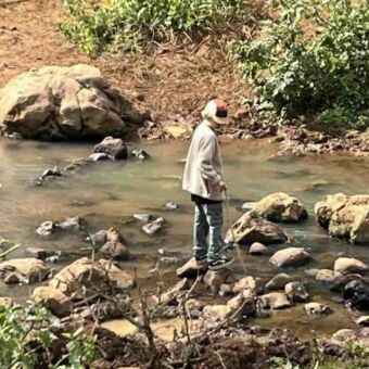 rivier met stenen waarop een jongen met een stok staat