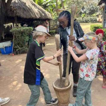 jongen en meisje die met een grote stamper mais malen in een houten kom. Een vrouw kijkt toe