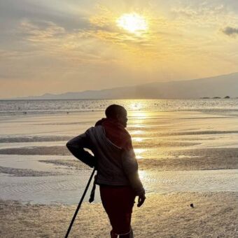 Een Masaï man leunend op zijn stok op een strand bij Lake Natron tijdens zonsondergang.