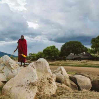 Masai man op grote rotsen met daarachter de Ruaha rivier en een accommodatie in Ruaha National Park Tanzania
