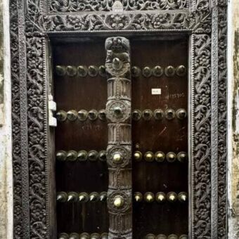 Een oude, houten deur in Stone Town met gedetailleerd houtsnijwerk en metalen versieringen.