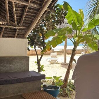 Een uitzicht vanaf een overdekte veranda met een rieten dak op een zandstrand en de blauwe zee op Zanzibar.