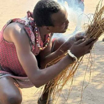 Masai man vuur probeert te maken en die in stro blaast waardoor er rook vanaf komt