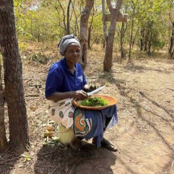 Vrouw zittend op een emmer snijdt groenten in een schaal