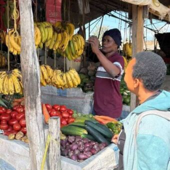 Marktkraam met groente en fruit met een man ervoor en in de kraam Stone Town