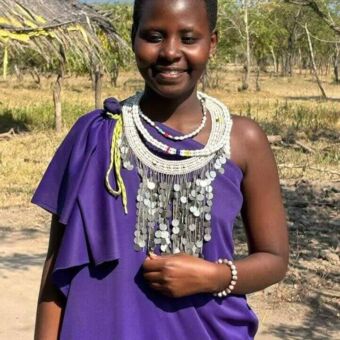 Lachende Tanzaniaanse vrouw in een kleurrijk paard gewaad en grote witte kettingen om haar nek