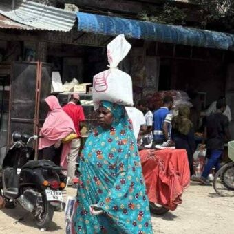 In blauw gekleed vrouw lopend met een grote witte zak op haar hoofd Zanzibar