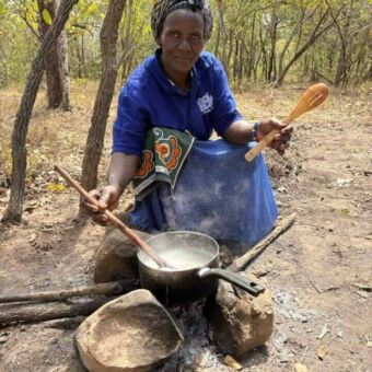 Vrouw die bij een vuurtje zit waarop een pan staat waarin ze roert