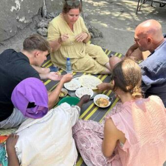 Gezin met dochter, zoon zittend op een kleed samen met eenTanzaniaanse vrouw waar ze het eten mee hebben bereidt