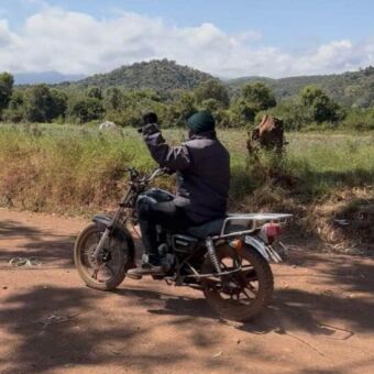 Man op een brommer op een rode zandweg in een groene omgeving in Tanzania