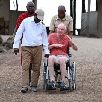 Medewerkers van een lodge praten met een man in een rolstoel terwijl ze hem voortduwen