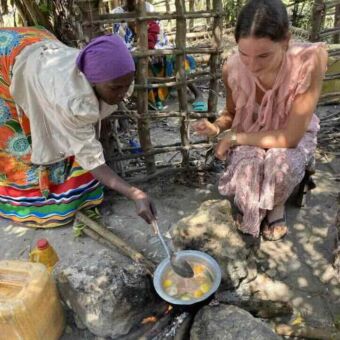 Jonge vrouw met Tanzaniaanse moeder die in een pot roert waarbij ze samen het eten bereiden