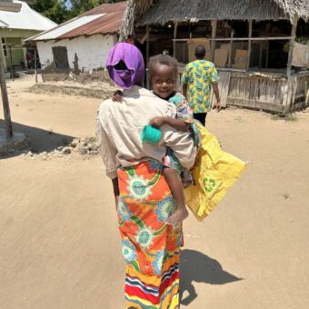 vrouw in kleurrijke kleding die van je af loopt met een baby op de arm die je aankijkt