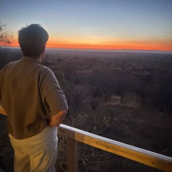 horizon kleurt oranje van de ondergaande zon en een vrouw staat op de veranda te kijken