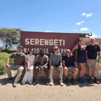 Een groep lachende reizigers zit op het welkomstbord van Serengeti National Park, Tanzania