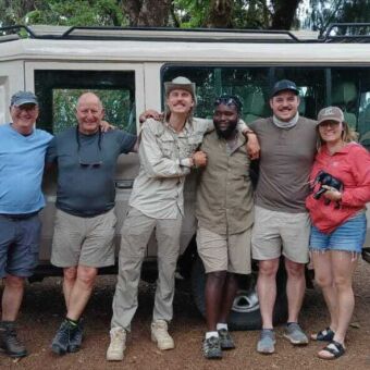 Een groep vrolijke reizigers met hun gids poseert samen voor hun 4x4 safariauto van Droomreis Tanzania