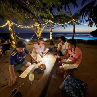 Familie zit 's avonds gezellig aan een houten tafel op het strand bij kaarslicht